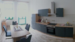 A modern kitchen with grey cabinets, a built-in oven, and a sink. There is a dining table with chairs and a vase of flowers. - Apartment I. First floor 82sqm, 2 bedrooms with balcony - Old Fire Station Görlitz City (Görlitz)