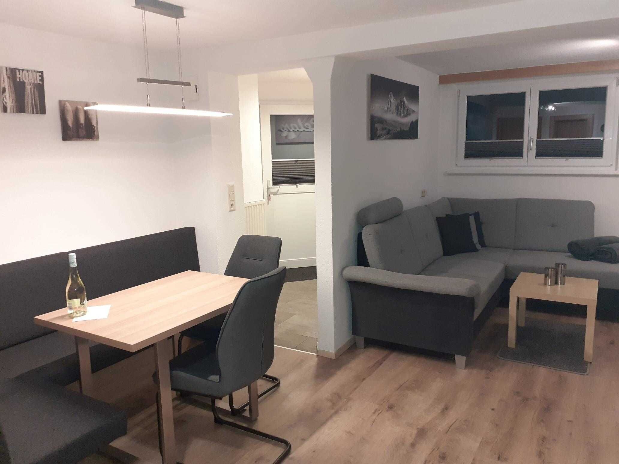 A modern living room with a sofa, a dining table, and a small coffee table. There is a bottle of wine on the table.