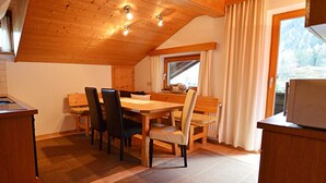 Tunnelmallinen keittiö, jossa on puupalkit katossa, ruokapöytä tuoleineen ja ikkuna, jossa on verhot.