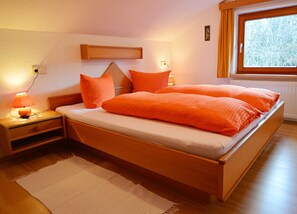 A bedroom with a wooden bed, two bedside lamps, a nightstand, a window with a view of trees, and a wooden headboard. - Vacation apartment cat. 4 1 - Active vacation apartments Pienz-Bobnar (Sautens)