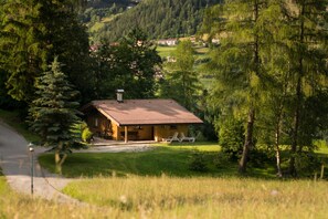 Una baita di legno con tetto in tegole, circondata da alberi e da un'area erbosa.