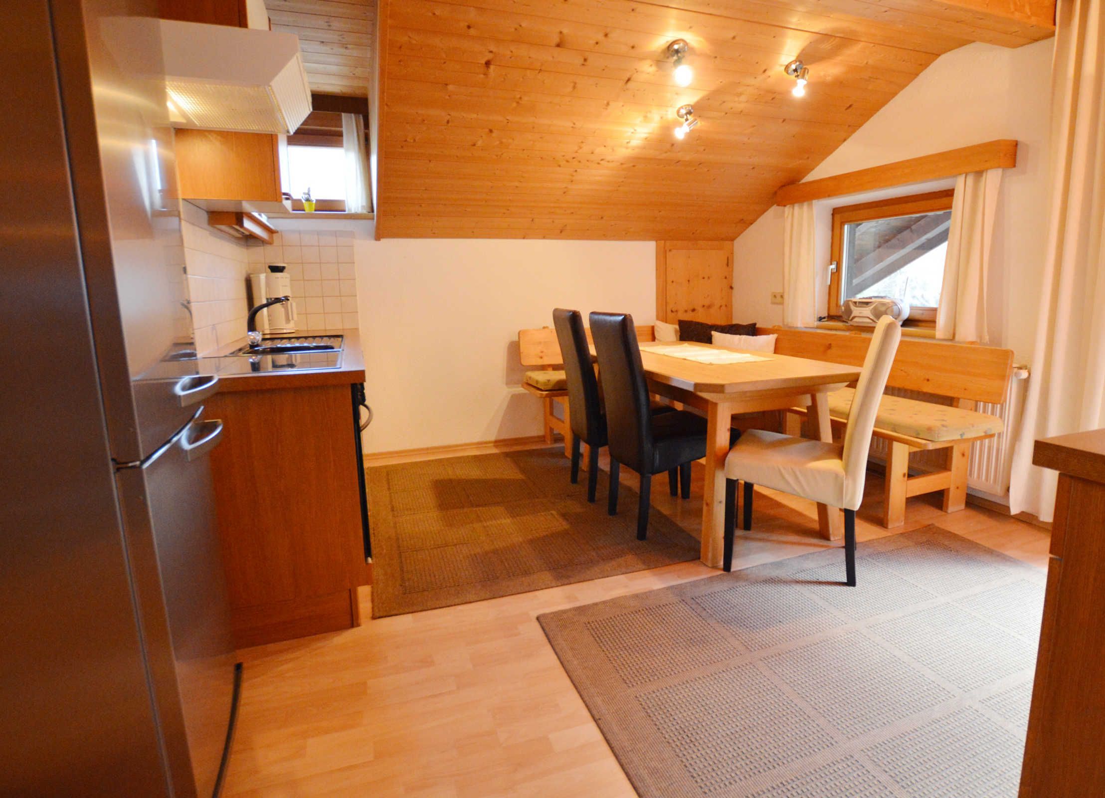 Une cuisine de taille réduite, équipée d’un réfrigérateur, de meubles de rangement en bois et d’un coin repas avec une table et des chaises.