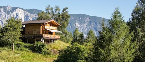 A wooden cabin with a balcony, surrounded by trees and mountains.