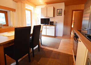 A kitchen with wooden cabinets, a microwave, a stove, and a dining area with chairs and a table. - Vacation apartment cat. 4 1 - Active vacation apartments Pienz-Bobnar (Sautens)