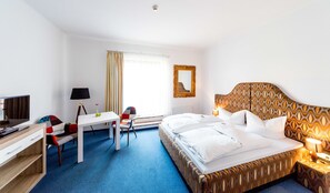 A hotel room with a bed, a desk, a chair, a lamp, and a window with curtains.