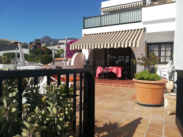 A rooftop terrace with a table and chairs, potted plants, and a view of the surrounding buildings.