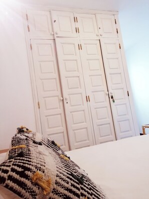 Une chambre à coucher avec un lit, un mur blanc et une armoire blanche à deux portes.