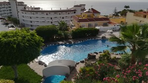 Ein Poolbereich mit freiem Blick auf das Meer, umgeben von Gebäuden und Grünflächen.