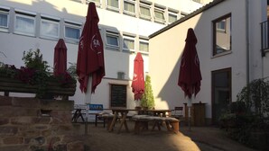 A courtyard with outdoor seating, red umbrellas, and a signboard listing food and drink options. - McMüller's Kemenate Fulda (Fulda)