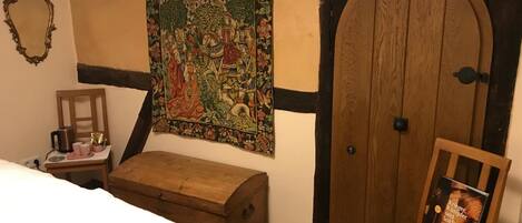 A bedroom with a wooden bed, a chest of drawers, a tapestry, and a wooden door.
