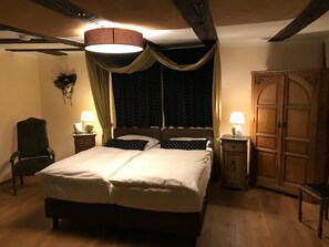 A bedroom with a large bed, two bedside tables with lamps, a chair, and a wardrobe. - McMüller's Kemenate Fulda (Fulda)