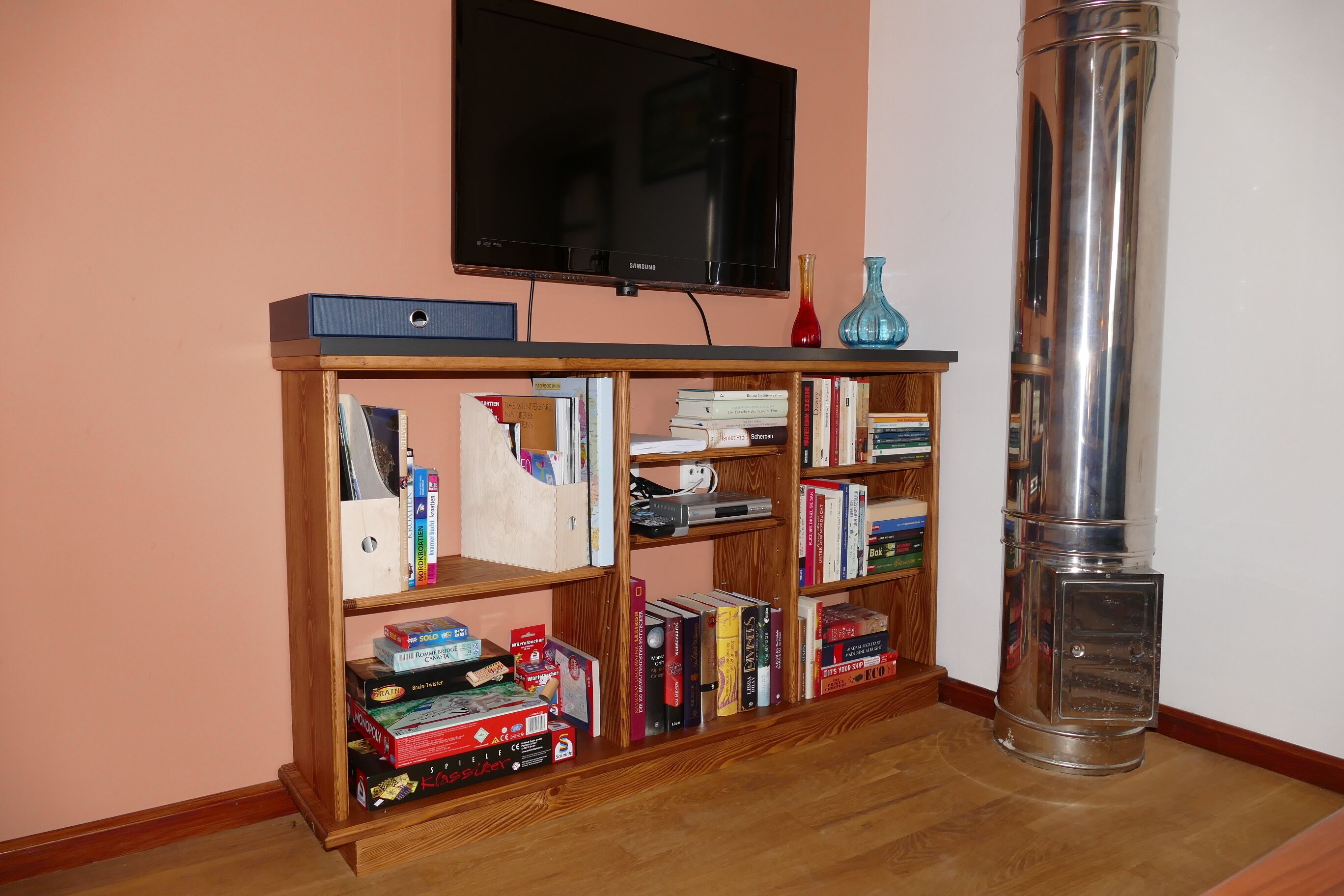Una habitación con una estantería de madera, un televisor y un objeto cilíndrico alto.