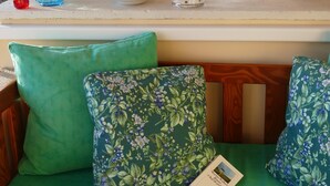 Une pièce avec une fenêtre donnant sur l’extérieur, une étagère ornée d’objets décoratifs et un banc recouvert d’un tissu vert agrémenté de coussins à motifs floraux.