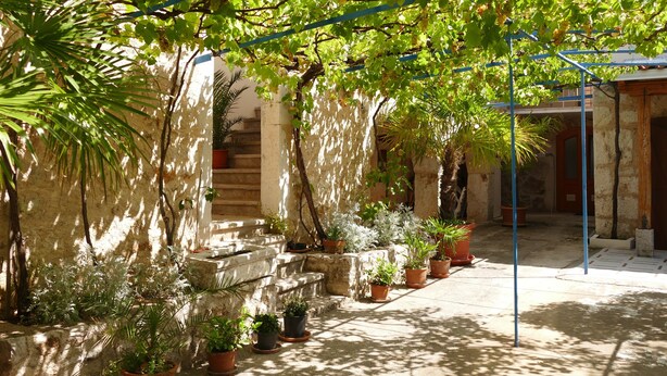 Une cour intérieure agrémentée de plantes en pot, d’un escalier en pierre et d’une pergola en métal.