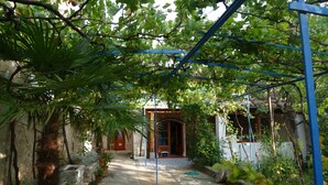 Une cour avec une pergola, des plantes en pot et l’entrée d’un bâtiment.