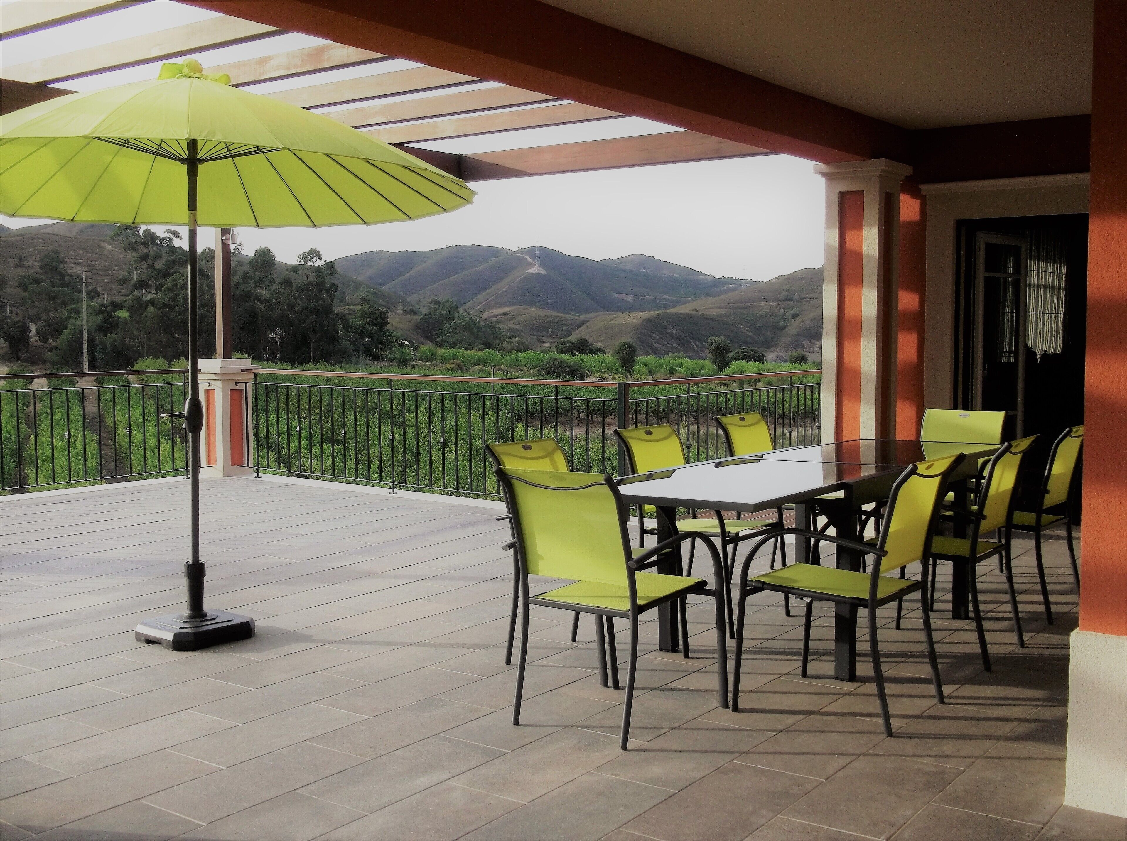 Une terrasse avec une table et des chaises, un parasol vert et une vue sur les montagnes.