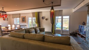 A living room with a sofa, a dining table, and a TV. There are windows with curtains and a view of the outdoors. - Luxurious villa with pool and idyllic lake landscape (Silves)
