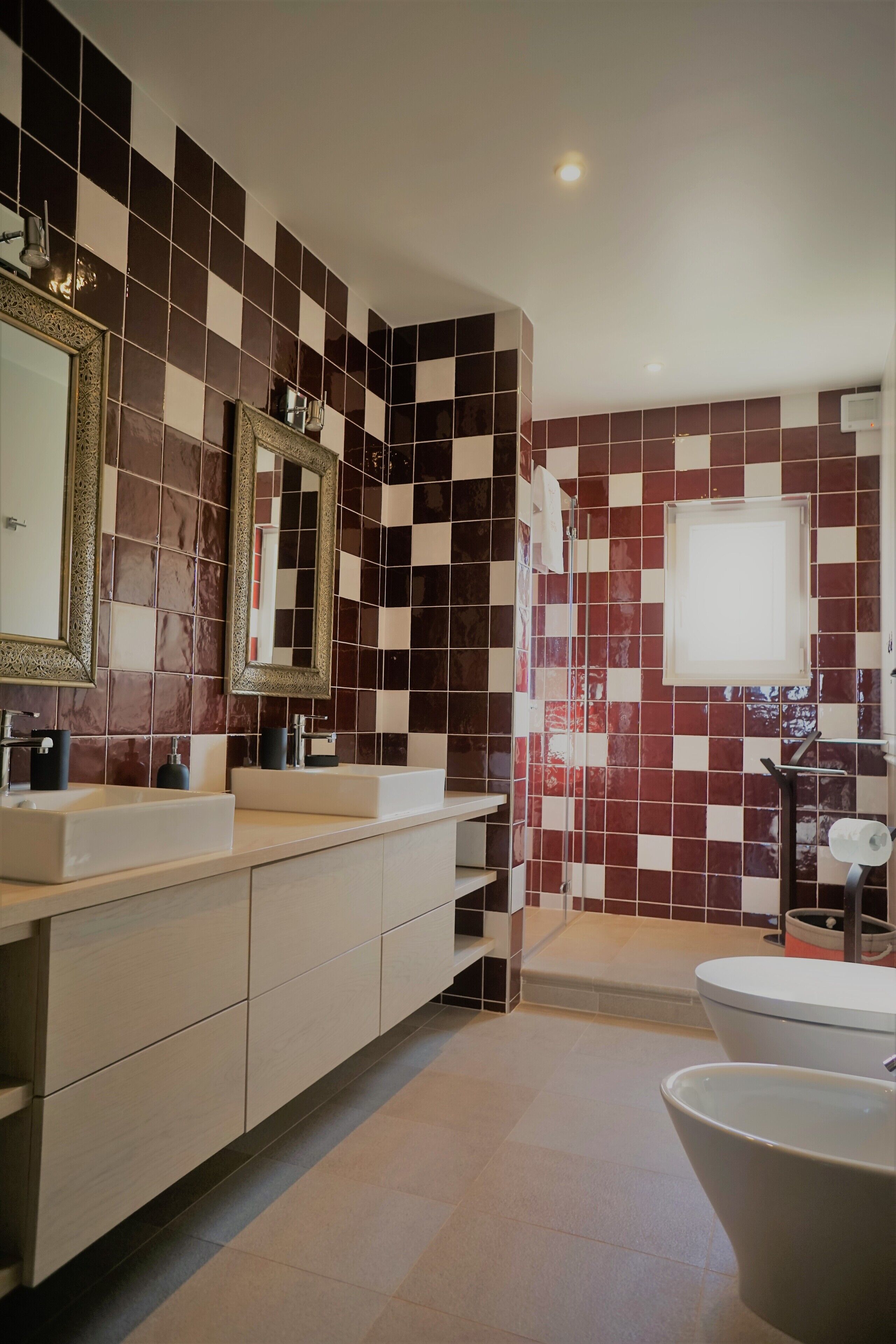 A modern bathroom with checkered tile walls, a double sink vanity, a large mirror, and a toilet.