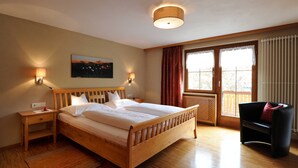 Ein Schlafzimmer mit einem hölzernen Bett, Nachttischen, einer Wandlampe, einem Fenster mit Vorhängen und Blick ins Freie.