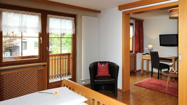 Ein Zimmer mit einem Holztisch, einem schwarzen Stuhl, einem Fernseher und einem Fenster mit Vorhängen.