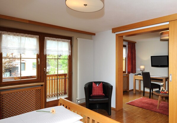 A room with a wooden table, a black chair, a TV, and a window with curtains.