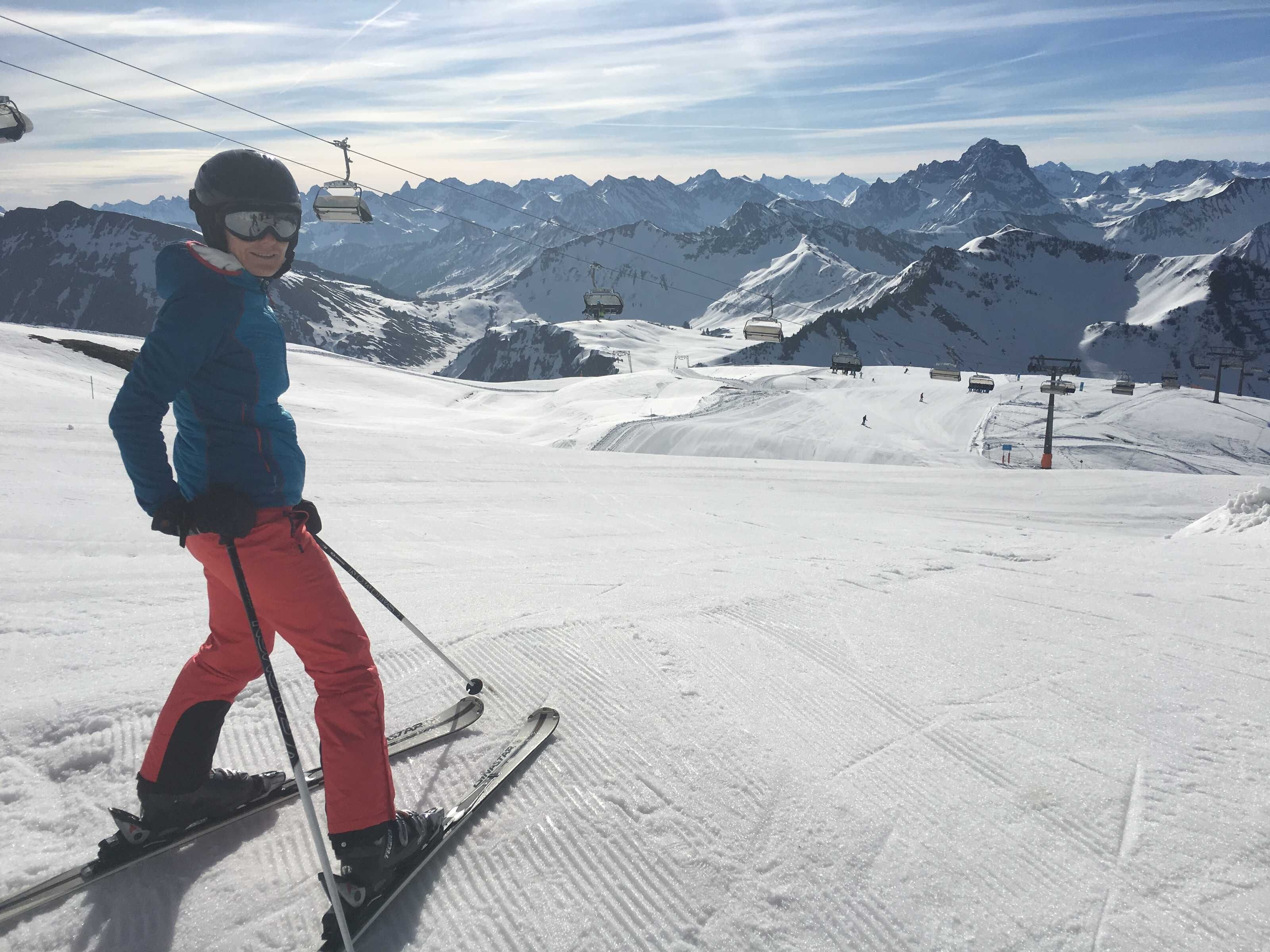 A person skiing on a snowy slope with a mountain range in the background and a ski lift in the distance.