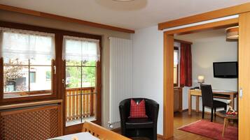 A room with a wooden table, a black chair, a TV, and a window with curtains.