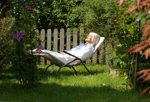 Une personne est allongée sur une chaise dans un jardin, avec une clôture en bois et de la verdure en arrière-plan.