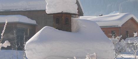 Un edificio cubierto de nieve con una chimenea, una estructura de madera y un cielo despejado.