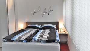 Ein modernes Schlafzimmer mit einem großen Bett, gestreifter Bettwäsche, einem Nachttisch und Vogeldekorationen an der Wand.