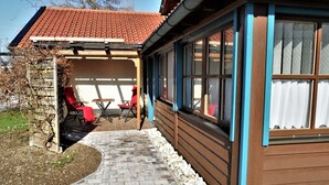 Ein überdachter Patio-Bereich mit Sitzgelegenheiten im Freien, ein Kiesweg und ein Gebäude mit großen Fenstern und einem Ziegeldach.
