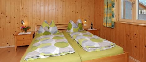 Et soveværelse med træpaneler, to senge, et natbord med lampe og et vindue med gardiner.