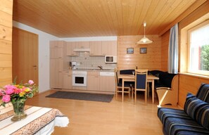 A compact kitchen with wooden cabinets, a microwave, and a dining area with a table and chairs.