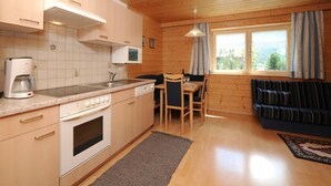 A compact kitchen with a microwave, stove, and coffee maker, a dining area with a table and chairs, and a sofa with a view of the outdoors. - Apartment 1 1 - Bishop Reingard (Schoppernau)