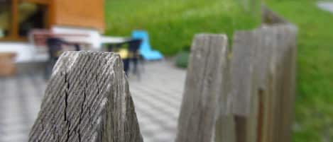 A wooden fence in a garden setting with a blurred background of a building and greenery.