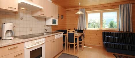 Cocina compacta con microondas, estufa y cafetera, zona de comedor con mesa y sillas, y sofá con vistas al exterior.
