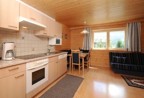 A compact kitchen with a microwave, stove, and coffee maker, a dining area with a table and chairs, and a sofa with a view of the outdoors. - Apartment 1 1 - Bishop Reingard (Schoppernau)
