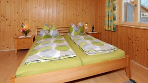 A wooden-paneled bedroom with two beds, a nightstand with a lamp, and a window with curtains. - Apartment 1 1 - Bishop Reingard (Schoppernau)
