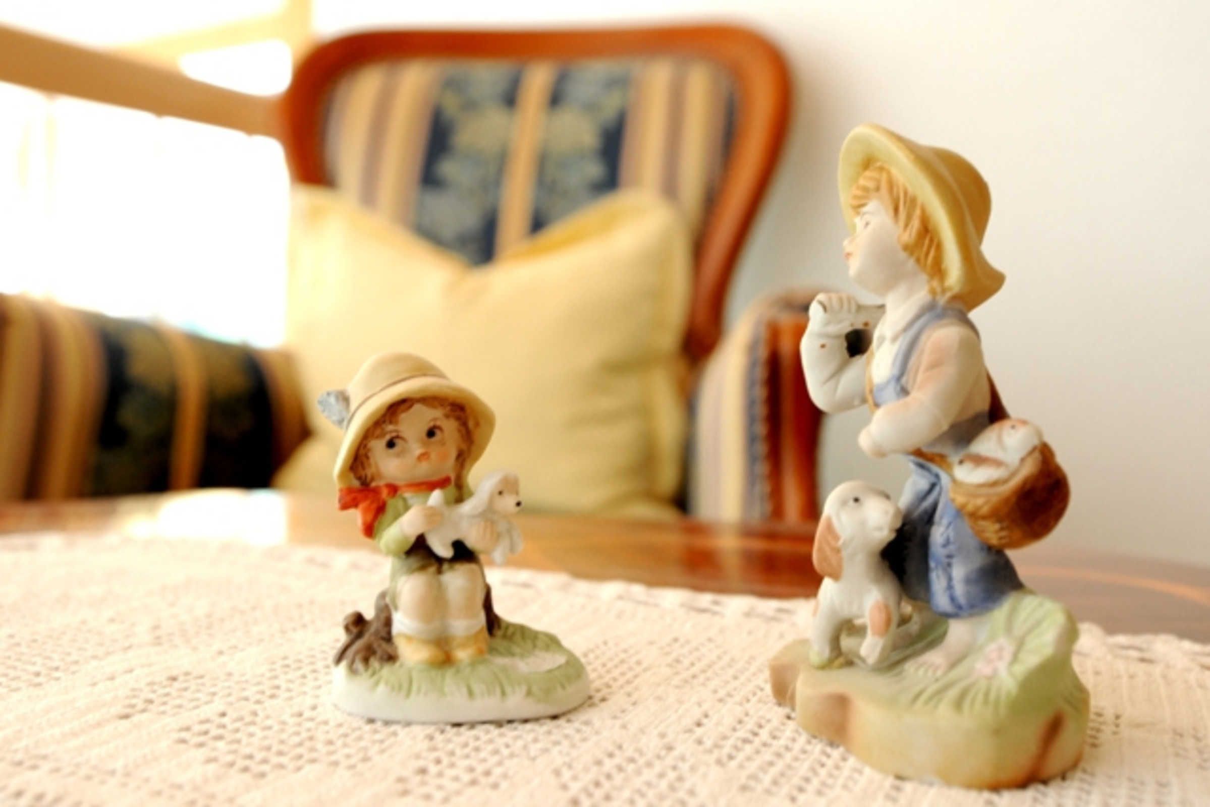 Due figurine su un tavolo, con una sedia e un cuscino sullo sfondo.