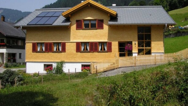 A two-story wooden house with a sloped roof, solar panels, and a wooden fence. - Apartment 1 1 - Bishop Reingard (Schoppernau)