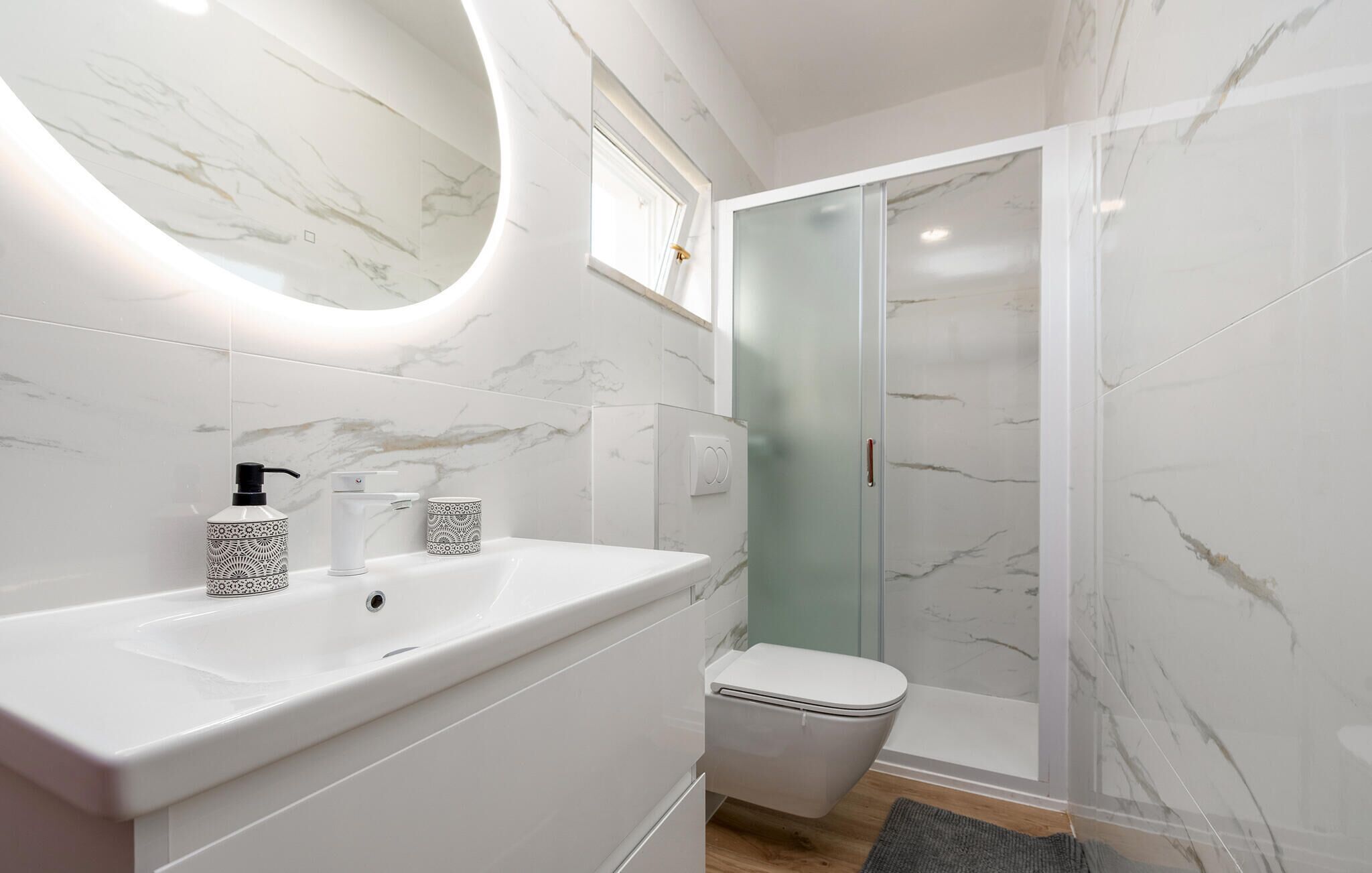 Een moderne badkamer met een witte marmeren wastafel, een glazen douchecabine en een toilet.