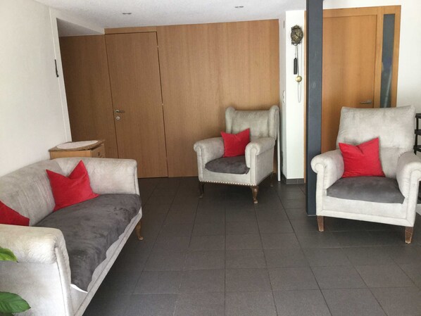 Een woonkamer met een bank, twee fauteuils, een houten garderobe en een klok aan de muur.