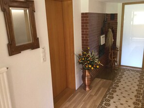 Un couloir avec une porte en bois, un miroir, un vase de fleurs, un mur en briques et un tapis à motifs.