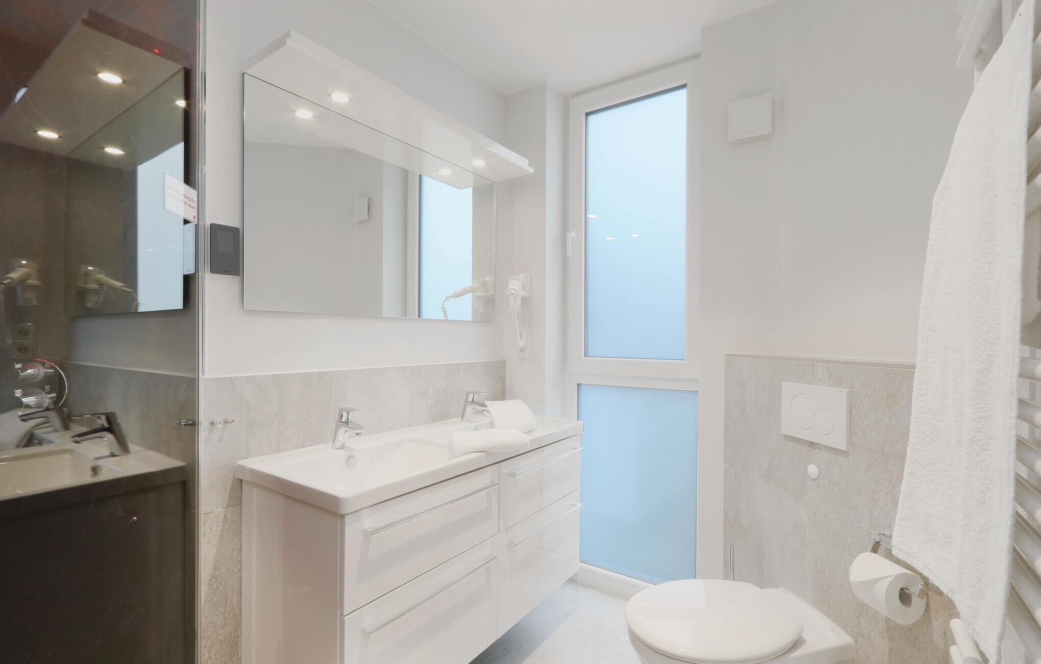 A modern bathroom with a large mirror, a white sink, a toilet, and a shower area.