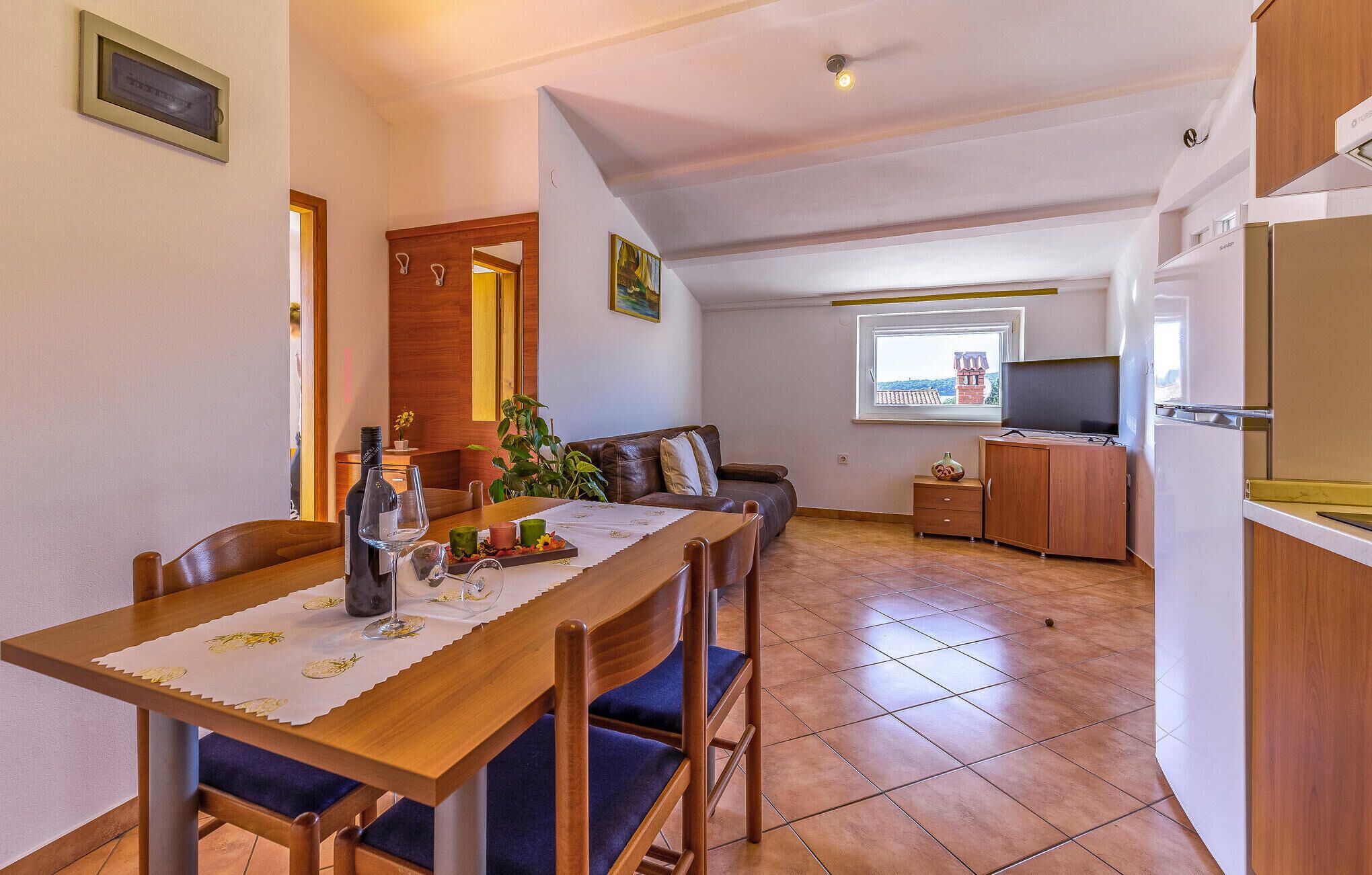 Un coin repas avec une table en bois, des chaises et une bouteille de vin. On aperçoit un canapé et un petit meuble en arrière-plan.