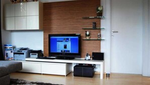 A modern living room with a flat-screen TV on a white entertainment unit, a wooden accent wall, and a white door. - Luxury Apartment Alpenblick ***** - Berghaus Tirol (Seefeld in Tirol)