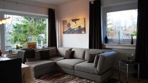 A modern living room with a sectional sofa, a large window with curtains, and a painting on the wall. - Luxury Apartment Alpenblick ***** - Berghaus Tirol (Seefeld in Tirol)