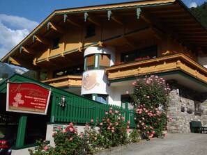 Un bâtiment de style alpin traditionnel, doté d’un balcon, d’une enseigne et agrémenté de magnifiques rosiers en fleurs.