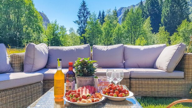 A wicker sofa with cushions, a glass table with a bottle, a potted plant, and a plate of strawberries.