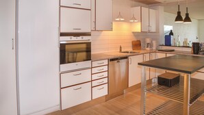 Une cuisine moderne avec des meubles blancs, un four encastré, un lave-vaisselle et des luminaires suspendus.